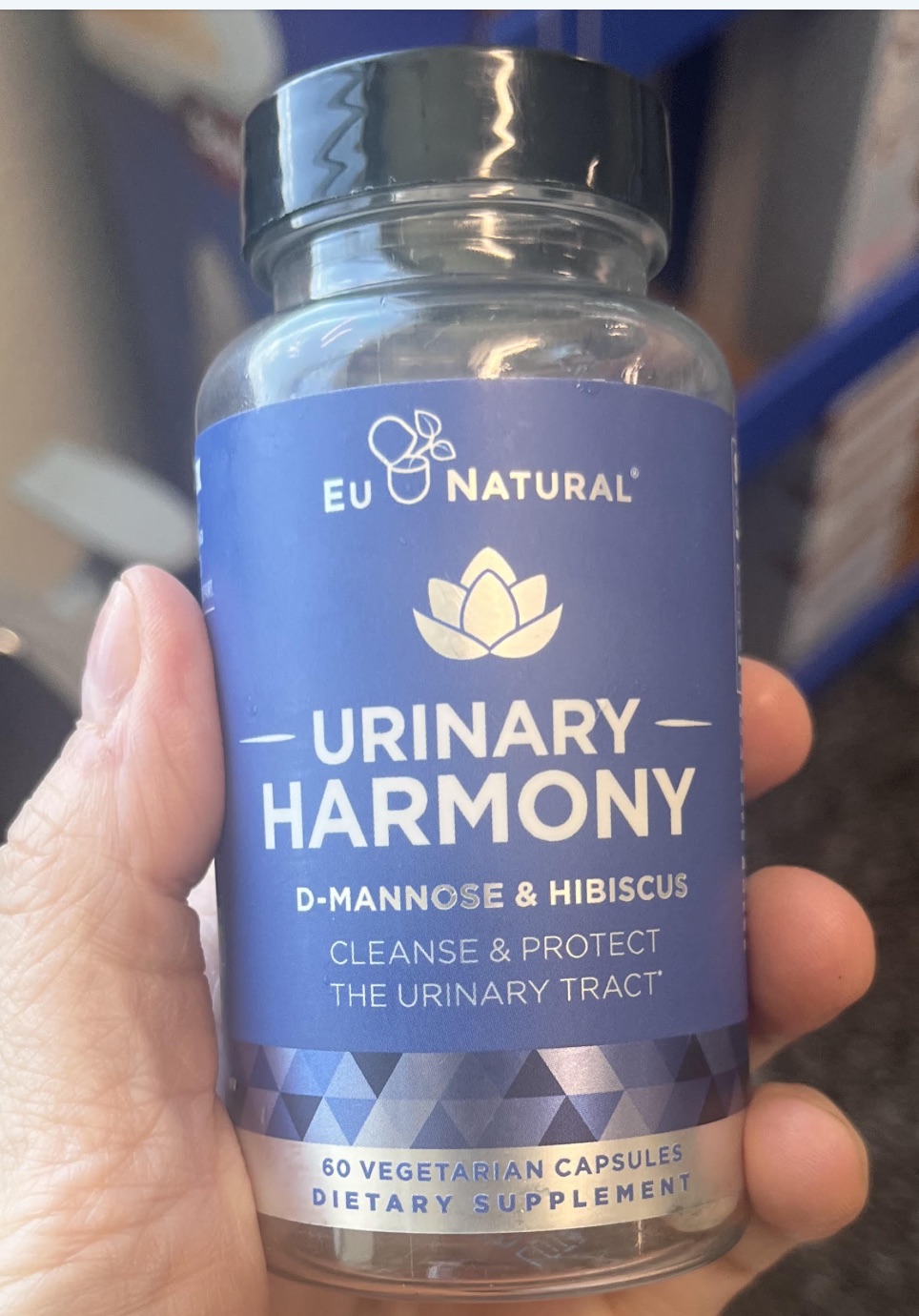 A hand holding a bottle of EU Natural Urinary Harmony labeled D-mannose and hibiscus