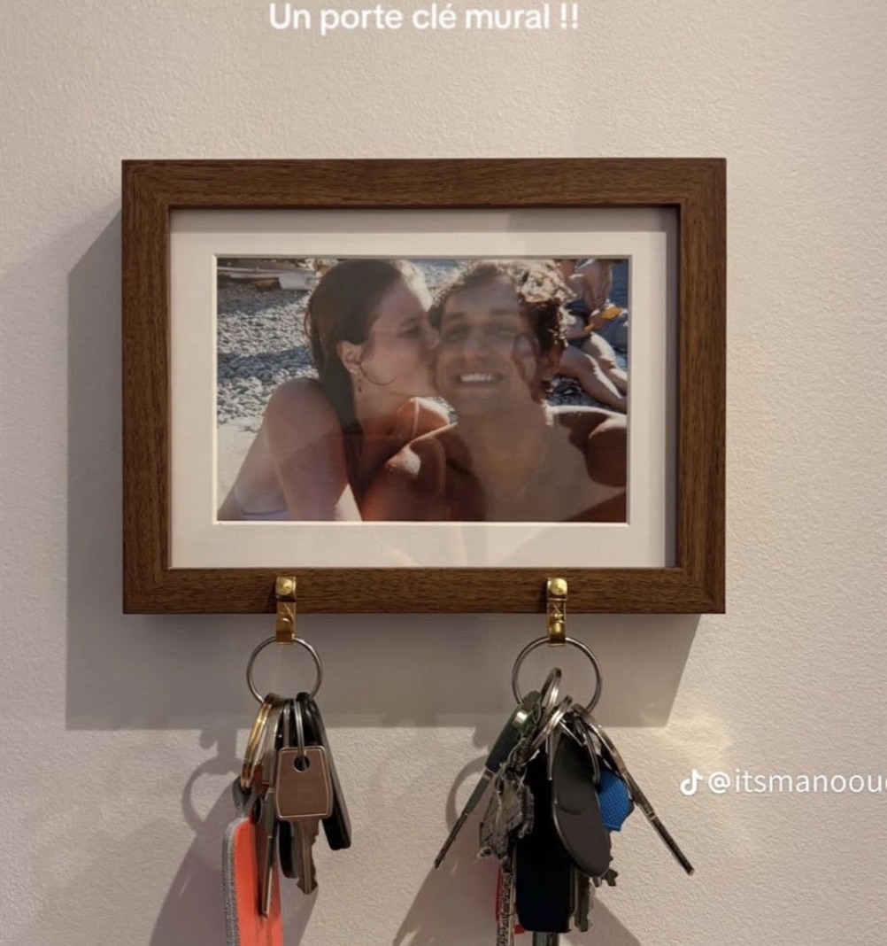Wooden picture frame holding a personal photo with two small brass hooks attached along the bottom for hanging keys