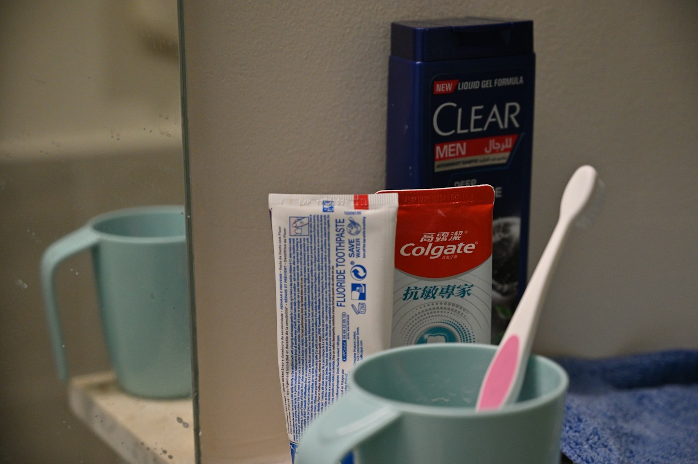Everyday toothpaste tubes and a toothbrush beside a bathroom mirror.