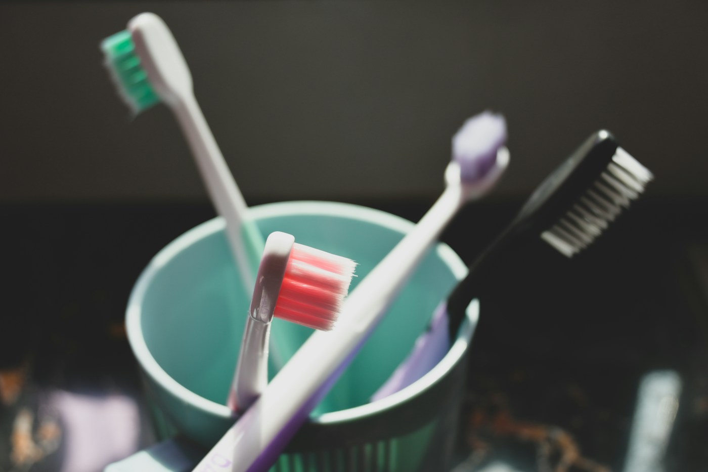 Several toothbrushes in a mint-green cup.