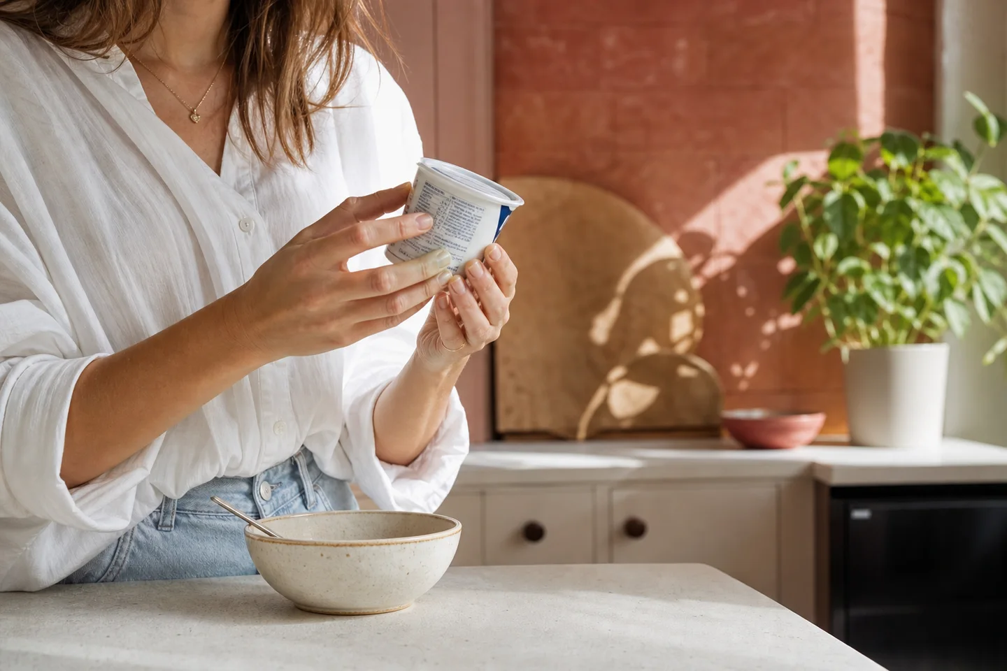 A woman reading the nutrition label on a yogurt container at a kitchen counter